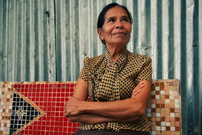 A Timorese woman sitting on a bench with with arms folded looking to her left