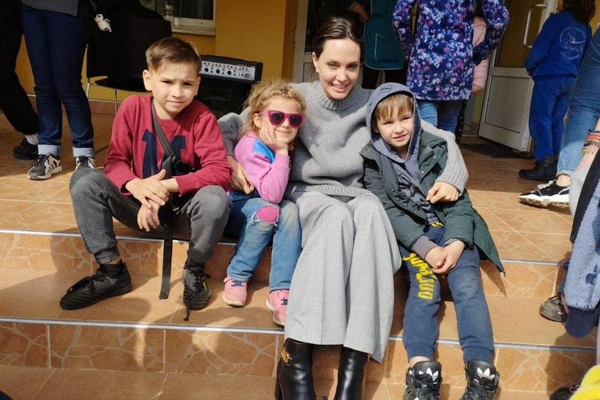 Женщина позирует фотографу с тремя детьми, сидящими на ступеньках.