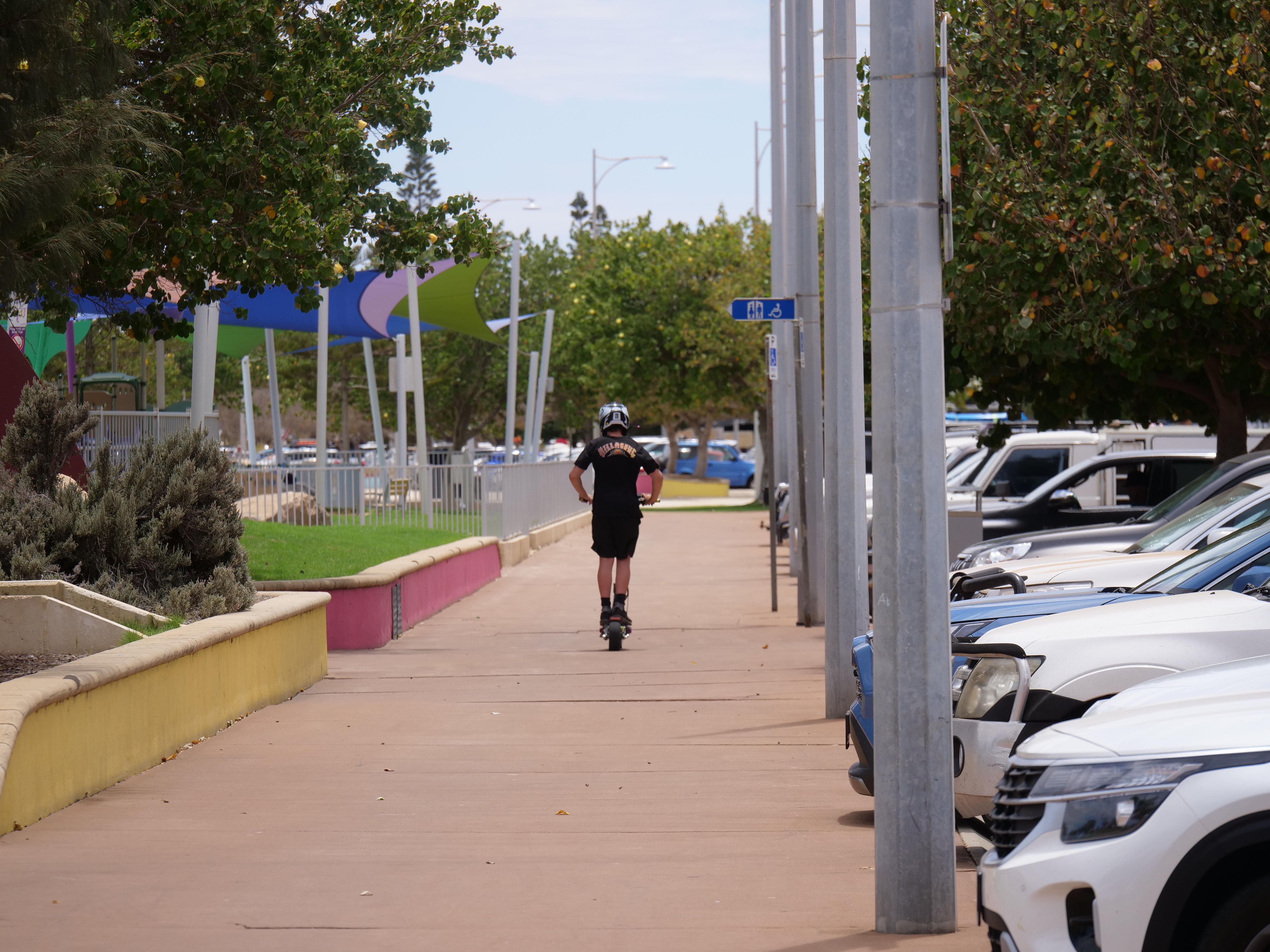 Un niño pequeño con casco se aleja de un camino en una escooter.