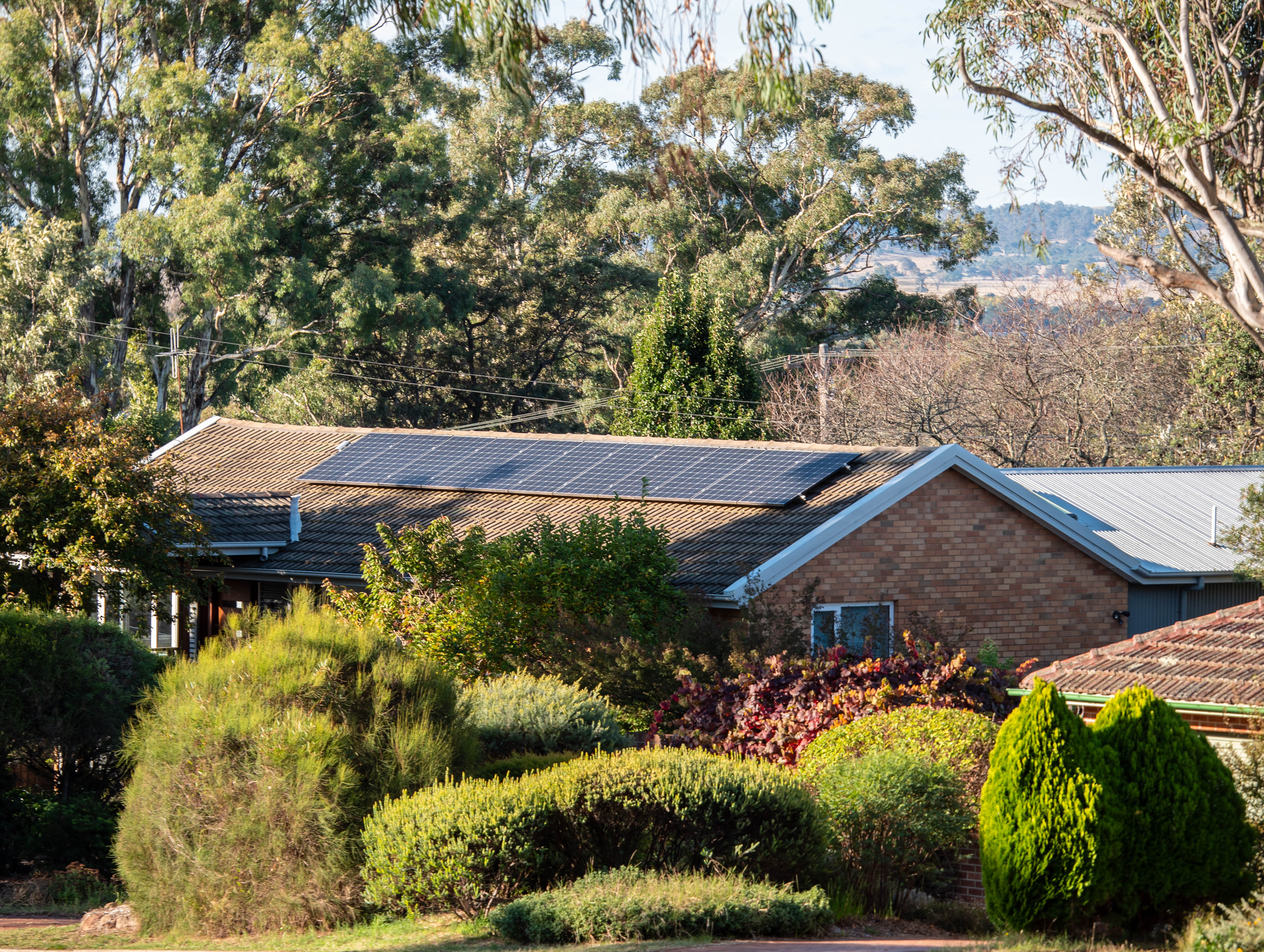 A red-brick home in a manicured garden with rooftop solar 