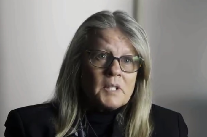 A screenshot of a video where Judy Mikovits is being interviewed. She is mid-sentence with a serious expression