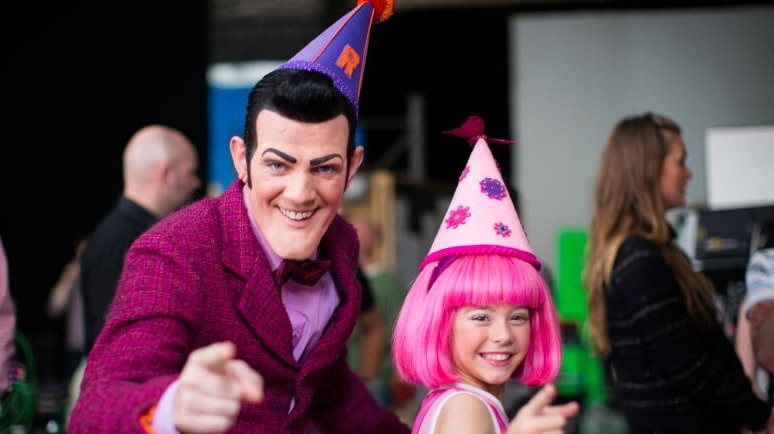 Stefan Karl Stefansson in costume as Robbie Rotten on LazyTown, points to the camera standing next to a young girl in a pink wig
