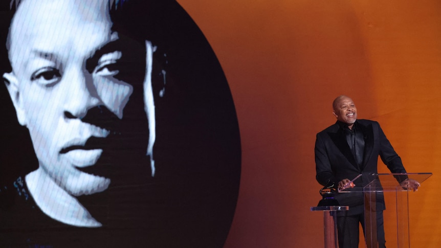 Dr. Dre standing on stage behind a lantern with a photo of his face beamed behind him