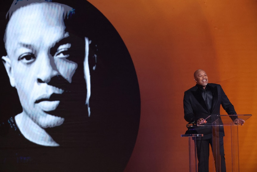 Dr. Dre standing on stage behind a lantern with a photo of his face beamed behind him