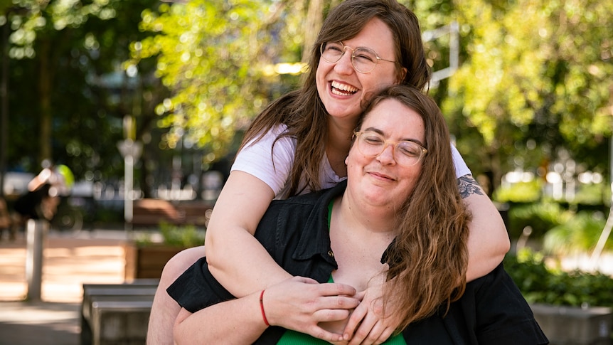 Freya, left, wraps her arms around Bec, right bottom, as they both beam while posing in a public park.