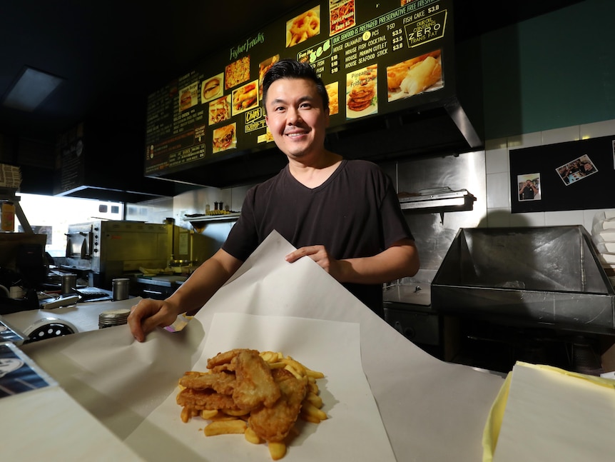 A man wraps up some fish and chips in a takeaway store.