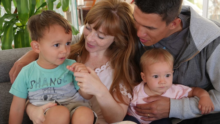 Man and woman sitting on lounge, singing to their baby daughter and young son for a story about why you should sing to babies.