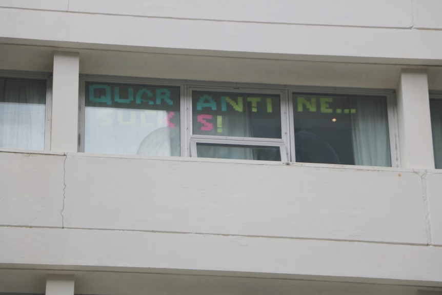 A close-up photo of post-it notes spelling out the words 'quarantine sucks!' in the window of a hotel in Perth.