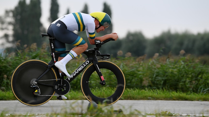 Luke Plapp rides a time trial bike on a road through some fields