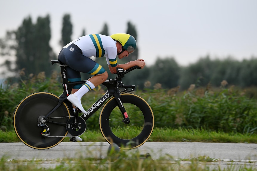 Luke Plapp rides a time trial bike on a road through some fields