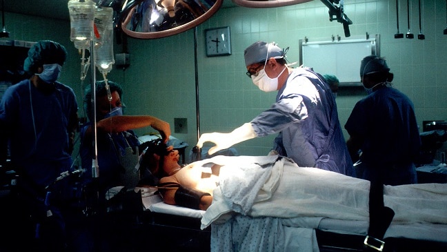 A woman lies on the operating table as surgeons prepare around her