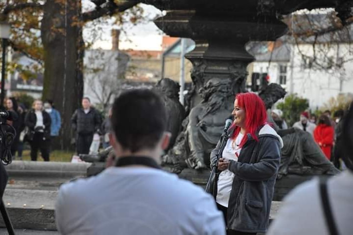 A woman addresses a crowd with a microphone in a street setting