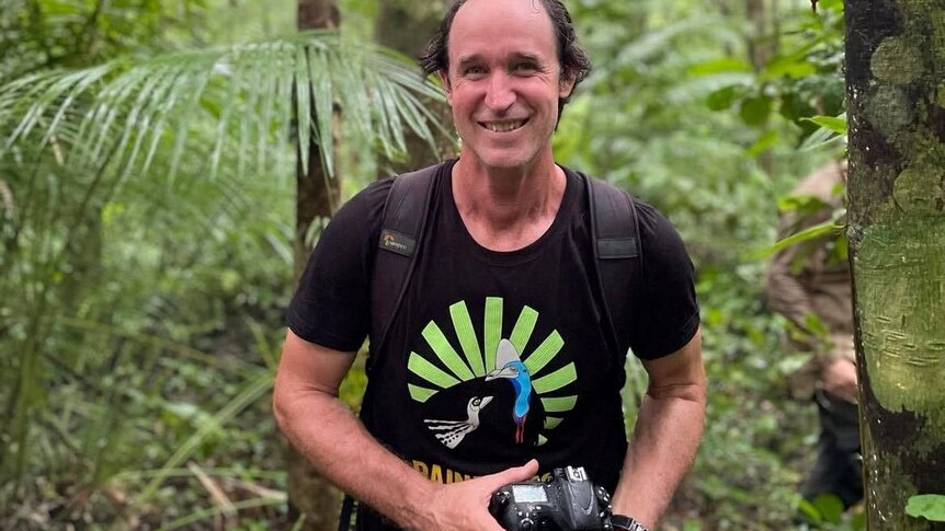 Man smiling while holding a camera in a rain forest 