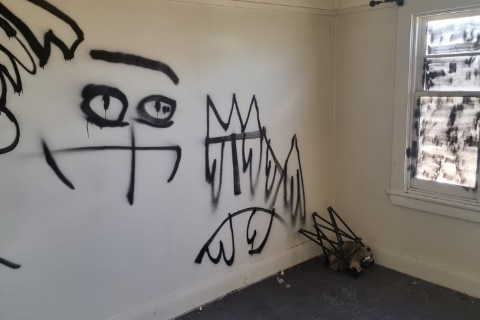 Black graffiti is sprayed on white interior walls and on a window.