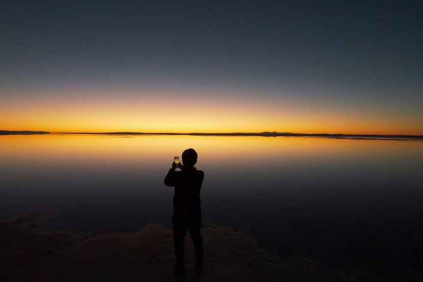 Un enfant prend une photo sur un téléphone portable d'un coucher de soleil avec le coucher du soleil en arrière-plan