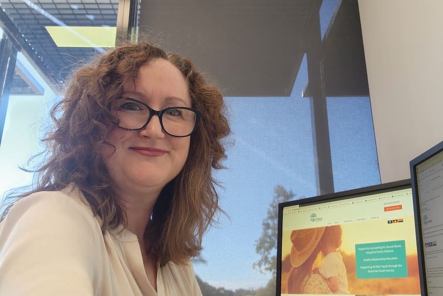 Woman sitting in front of a computer wearing black glasses.