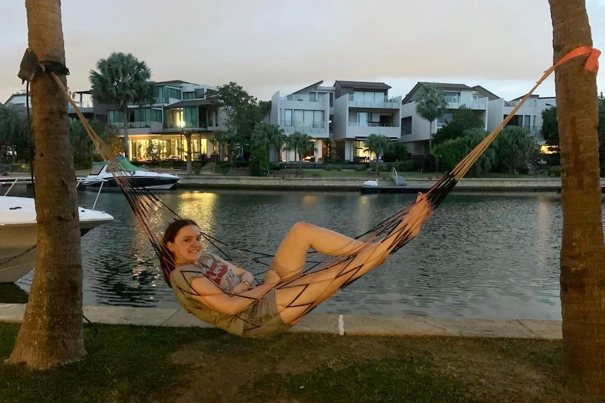 A teenage girl lies in a hammock next to a river with houses behind