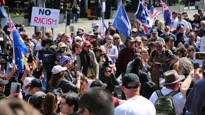 A crowd of people with australian flags and a sign thats reads 'NO to racism'