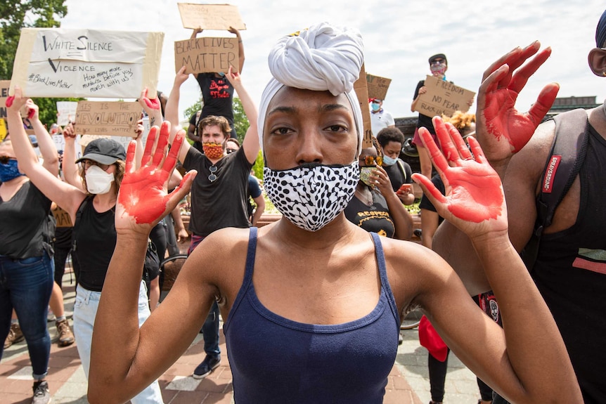A woman in a face mask holding her hands up with red paint on her palms