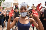 A woman in a face mask holding her hands up with red paint on her palms