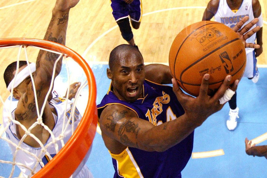 In a photo taken from next to the rim, Kobe can be seen jumping and lifting the ball towards the hoop while being defended.