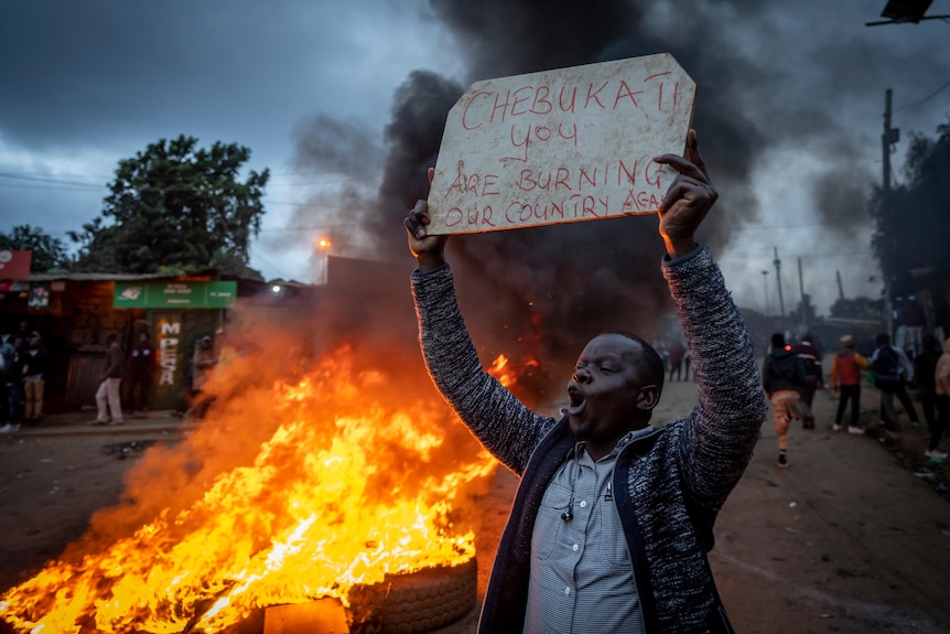 A supporter of presidential candidate Raila Odinga holds a placard in front of a burning pile of tyres.