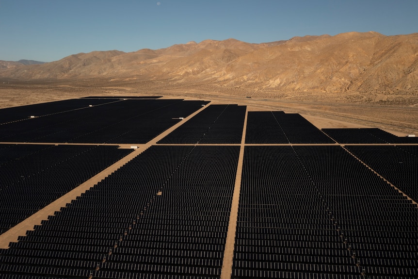 Hundreds of black solar panels next to desert and small mountains