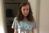 A teenage girl wearing a grey Snoopy shirt stands in a hallway.