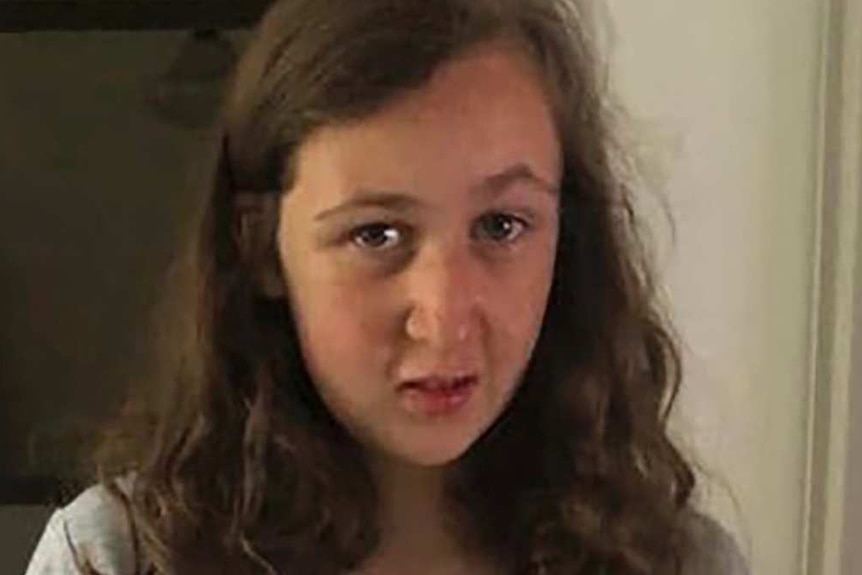 A teenage girl wearing a grey Snoopy shirt stands in a hallway.