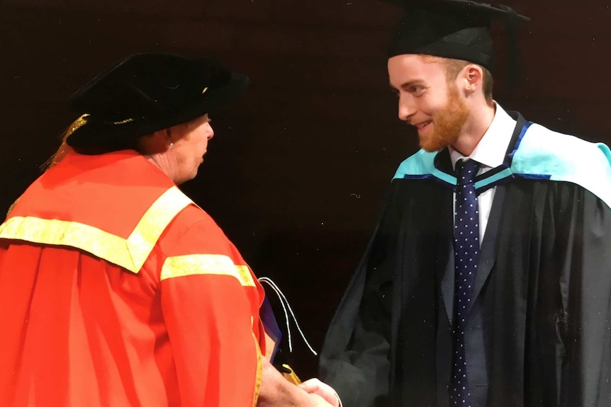 A young man in a graduation gown shakes the hand of a woman onstage