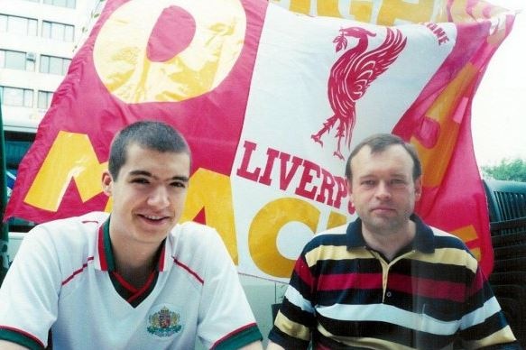 Two men sit in front of a flag