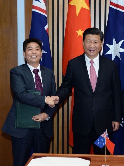 Two men shaking hands in front of Australian and Chinese flags.