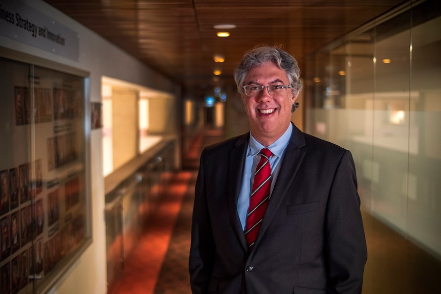 Professor Fabrizio Carmignani stands in a hallway smiling wearing a suit and red tie