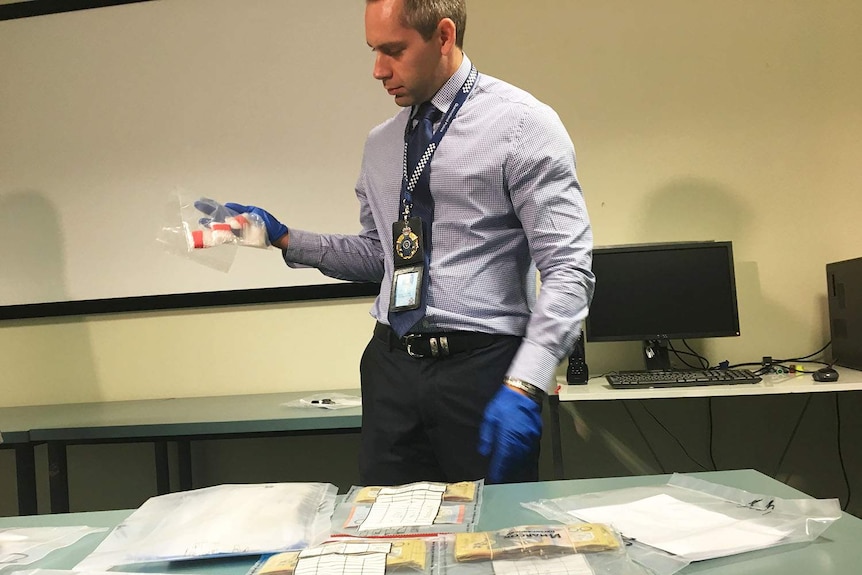 Police officer shows cash, drugs and other evidence seized in a bust in 2017 near Rockhampton in central Queensland.