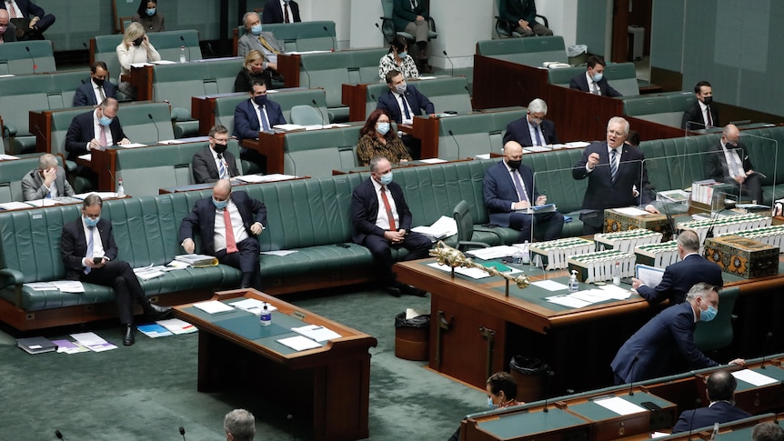 Scott Morrison points at the opposition, with several ministers sitting socially distanced on a bench behind him, wearing masks.
