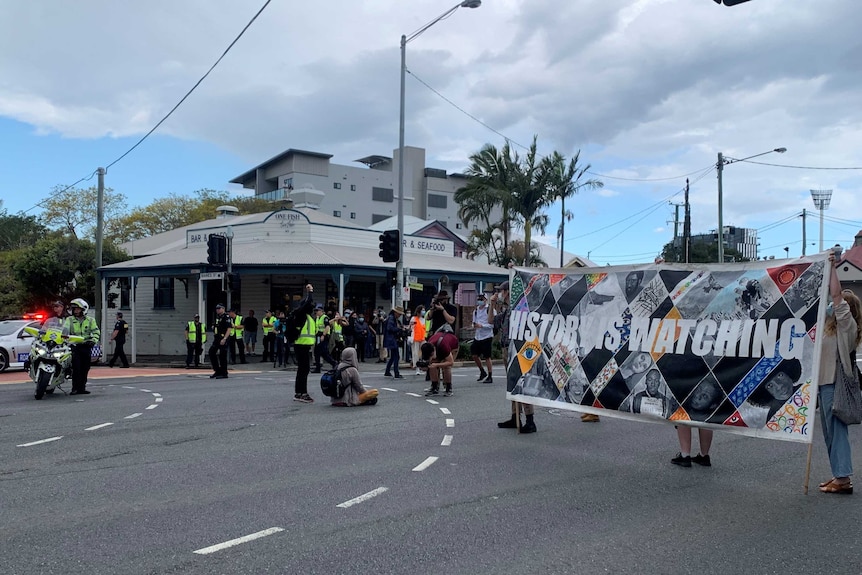 A man sits on the street with police nearby at a protest.