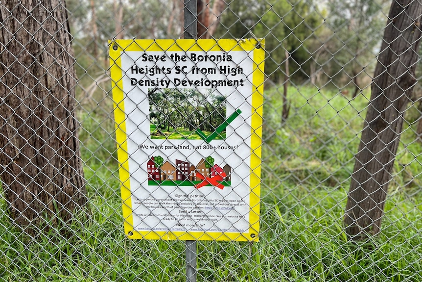 A sign attached to a wire fence with grass and trees in the background
