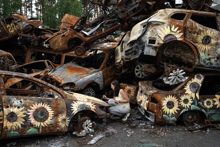 A Ukrainian artist Olena Yanko paints sunflowers on cars which were destroyed by Russian attacks in Irpin.