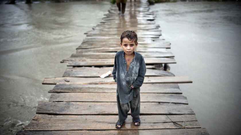 A Pakistani child stands on a wooden bridge surrounded by floodwaters