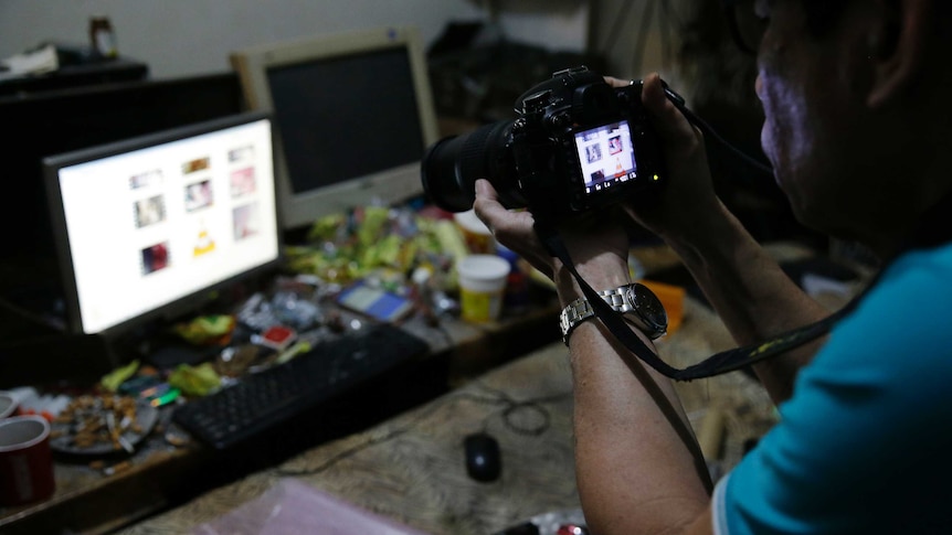 A Filipino police investigator takes a picture of the computer of suspected child exploitation operator David Timothy Deakin.