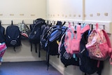 school backpacks  being held up by hooks on a wall