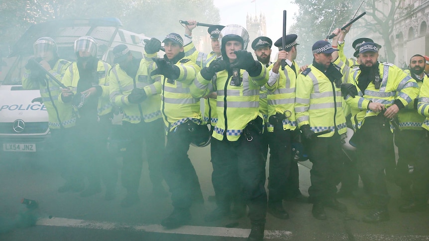 Police officers raise their batons as a smoke bomb goes off