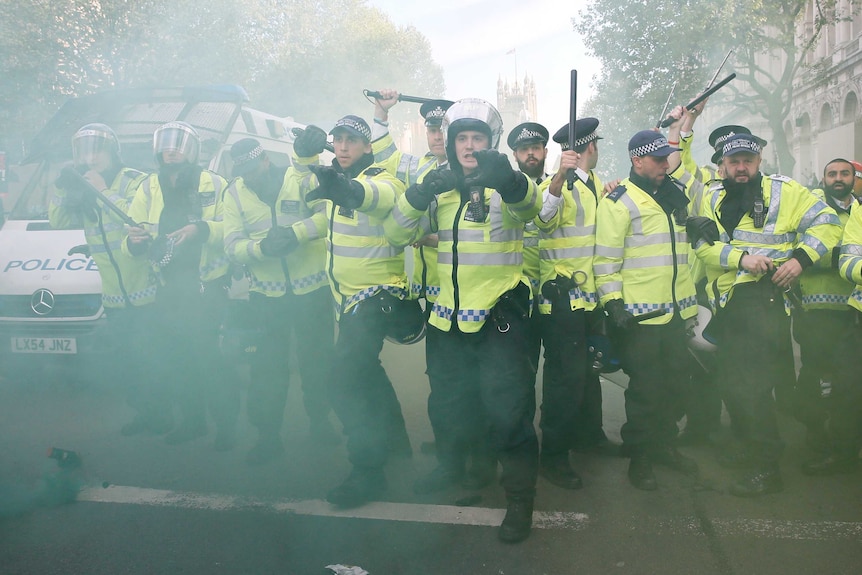 Police officers raise their batons as a smoke bomb goes off