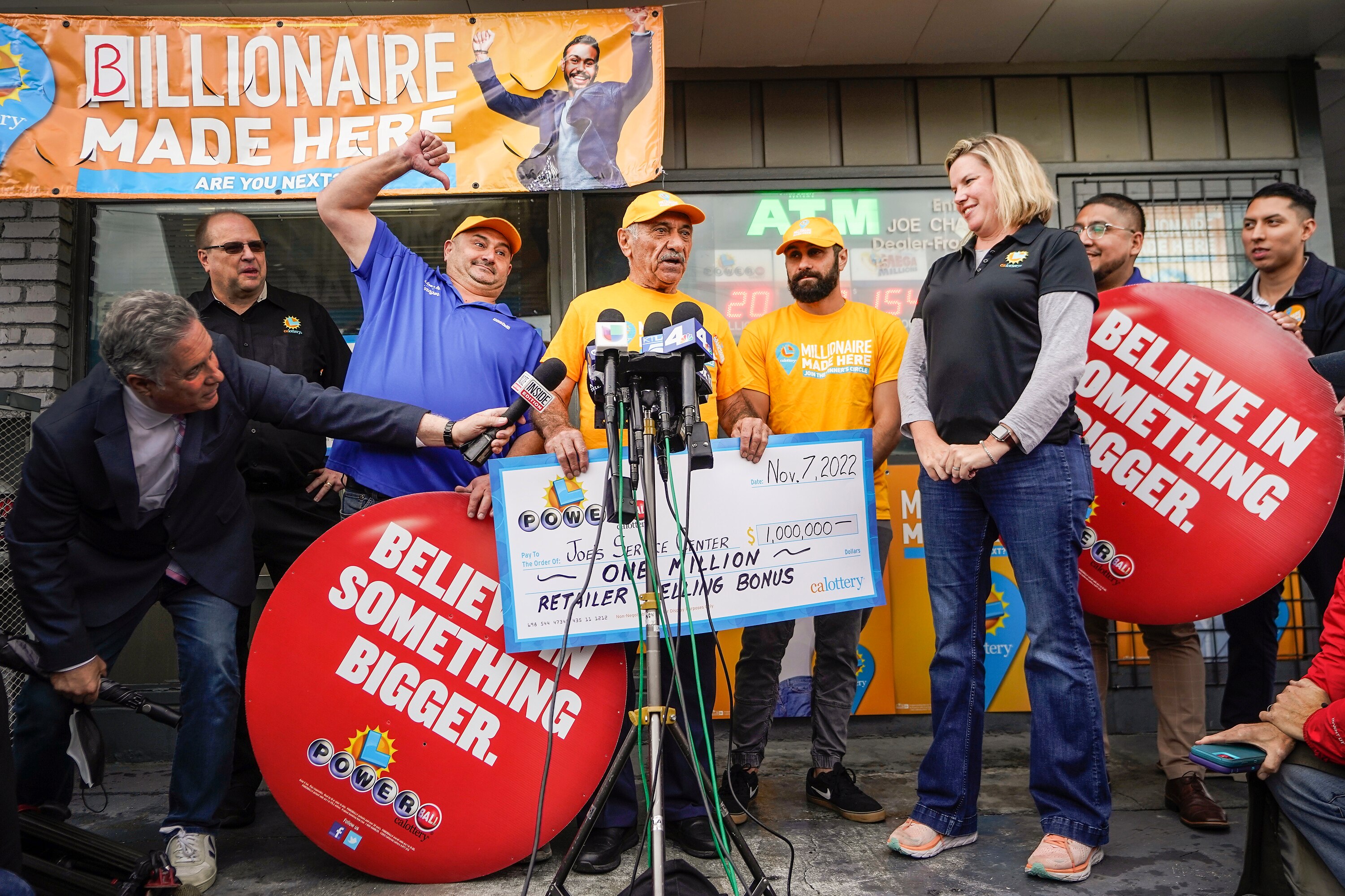 A man holds a check in front of microphones as people cheer around him. 
