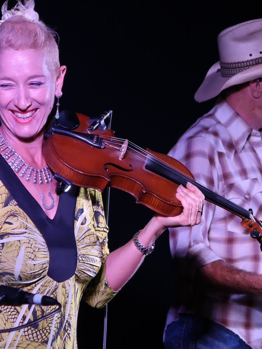 A woman holding her violin on stage.