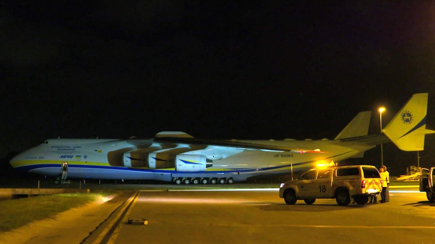 The world's largest plane, the Antonov An-225 Mriya, on the tarmac at Perth Airport in darkness with a car in the foreground.
