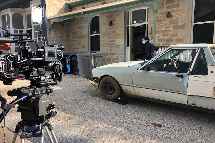 A camera films a person by an old ute in front of a building.