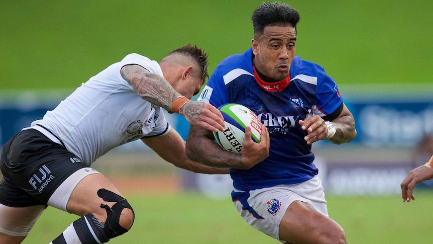 One man is tackling another man holding a rugby ball.