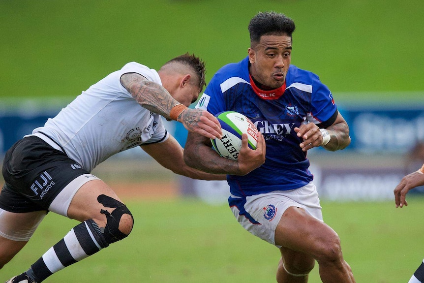 One man is tackling another man holding a rugby ball.