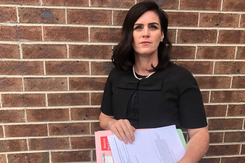 Shari Liby wears a black top and holds folders and documents.